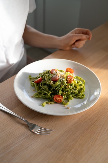 Cerca de mujer hizo pasta fettuccine con salsa pesto para el almuerzo, sentado en la mesa en la cocina de casa.