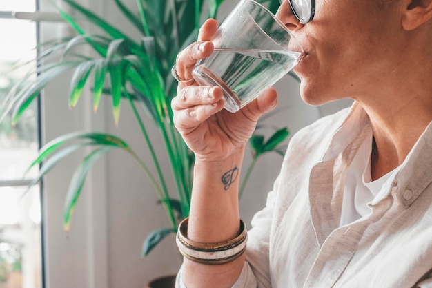 Cerca de una mujer joven bebiendo un vaso de agua fresca en la habitación doméstica en casa