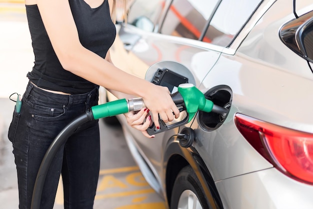 Cerca de una mujer joven poniendo gasolina en su coche en una gasolinera