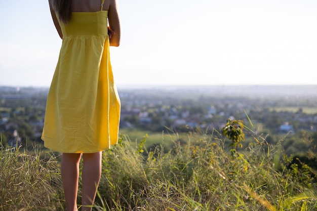 Cerca de una mujer joven en vestido amarillo de verano de pie al aire libre.