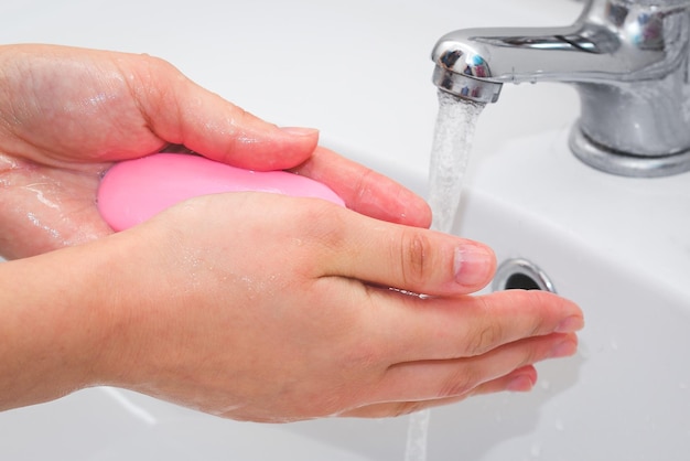 De cerca. Una mujer se lava las manos con jabón con agua corriente en el baño.