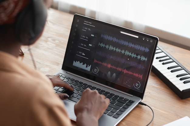 Cerca de la mujer músico afroamericano con ordenador portátil con software de edición de sonido mientras compone música en casa, espacio de copia
