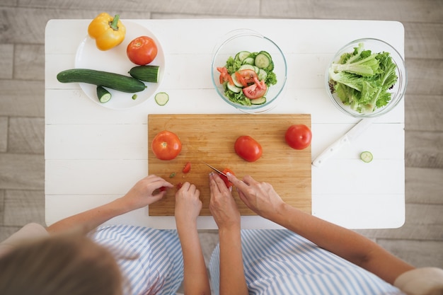 Cerca de una mujer y una niña cortando verduras para ensalada en la cocina