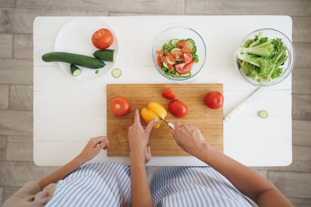 Cerca de una mujer y una niña cortando verduras para ensalada en la cocina