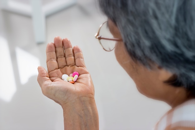 Cerca de mujer senior con pastillas y vaso de agua en casa, tomar medicamentos.