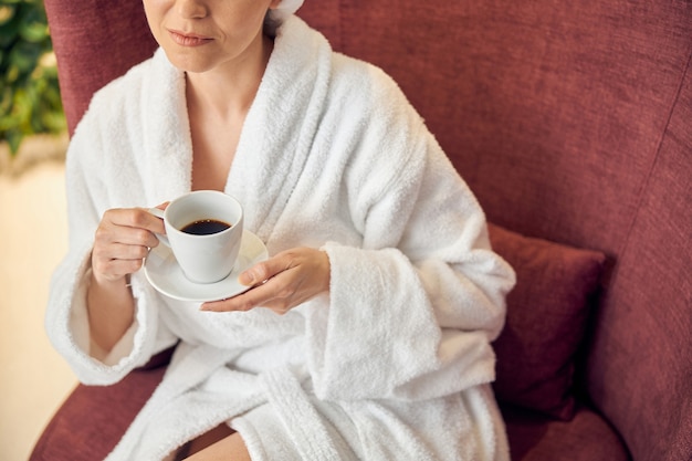 Cerca de una mujer sosteniendo una taza de café negro y un platillo en sus manos