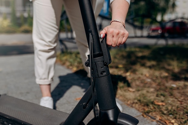 Cerca de una mujer con traje blanco doblando su scooter eléctrico después de un paseo mientras está de pie en el parque de la ciudad