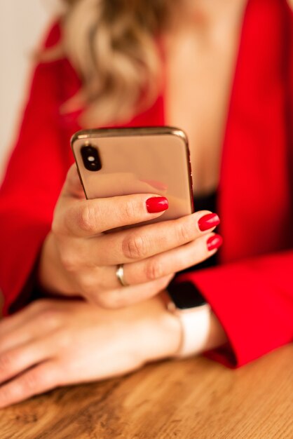 Cerca de una mujer en traje rojo con teléfono móvil inteligente. Blogger con manicura roja