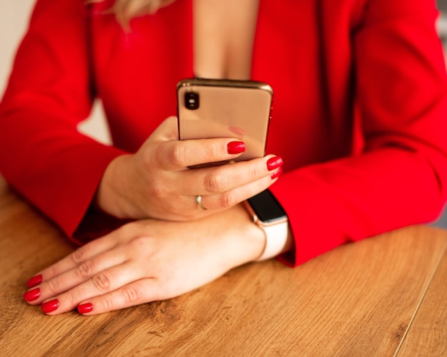 Cerca de una mujer en traje rojo con teléfono móvil inteligente. Blogger con manicura roja