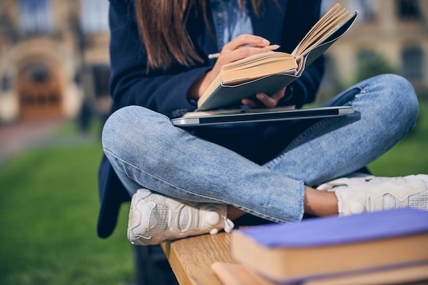 Cerca de mujeres en ropa casual sentado en el banco con libros y escritura