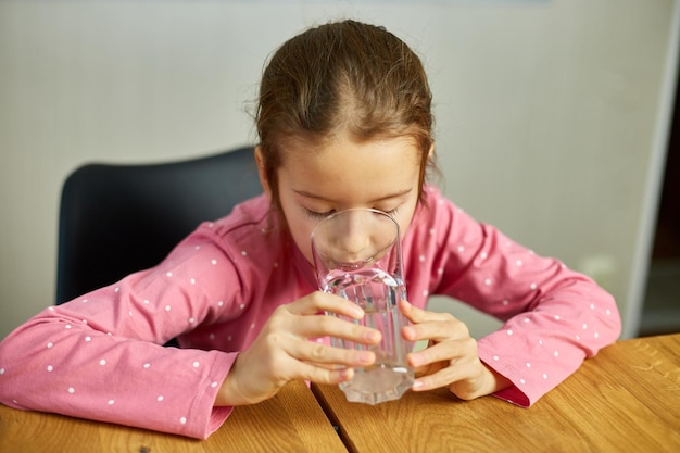 Cerca de una niña feliz bebiendo un vaso de agua dulce en la cocina