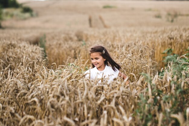 Cerca de niña feliz con largo cabello rubio corriendo hacia la cámara a través del campo de cebada.