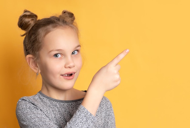 Cerca de una niña pensativa mirándote y señalando con el dedo un espacio vacío para el texto. Niño posando con el telón de fondo de una pared amarilla en el estudio. Bandera. Publicidad.