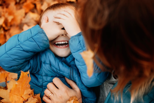 Cerca de un niño feliz riendo mientras oculta su rostro jugando con su madre mientras la madre le hace cosquillas al aire libre.