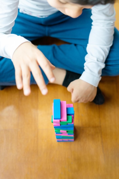 Cerca de niño jugando colorido juego de torre de pila de bloques de madera para niños en casa