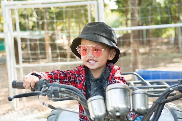 Foto cerca de un niño con sombrero y gafas de moda. él monta un quad en la granja está de buen humor.