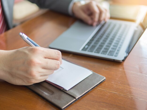 Cerca de la nota de la escritura del hombre de negocios y usando una computadora portátil en la oficina