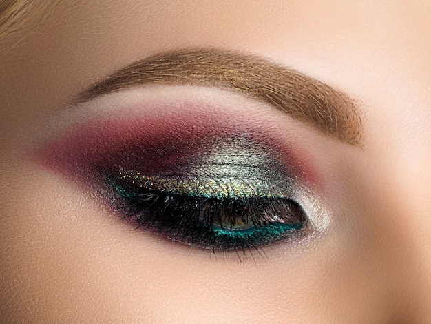 Cerca del ojo de mujer hermosa con maquillaje de ojos ahumado multicolor. Maquillaje de moda moderna.