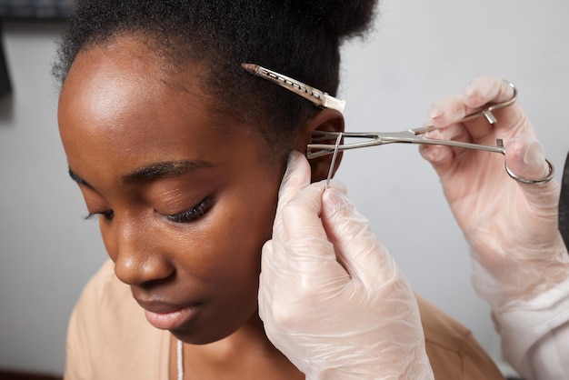 Cerca de la oreja de una mujer perforada en la oreja para el tratamiento del dolor en algún lugar de su cuerpo por un médico chino