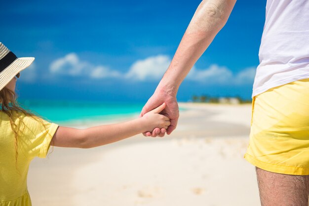 Cerca del padre y la pequeña hija cogidos de la mano en la playa