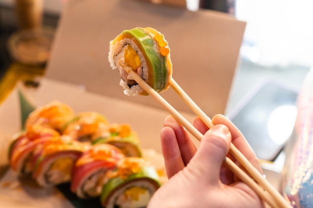 cerca de palillos que toman parte del rollo de sushi en el restaurante de mesa. comer rollo de sushi con palillos.