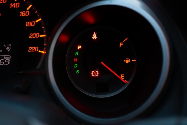 Cerca del panel del medidor con la aguja apuntando a E sobre fondo negro, el coche se ha quedado sin gasolina