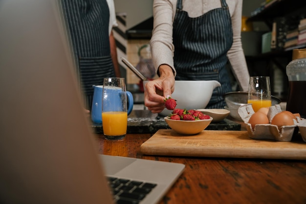 Cerca de una pareja de ancianos horneando en la cocina con una laptop