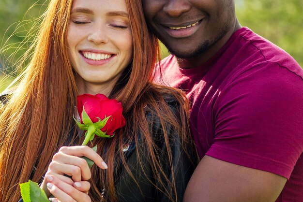 Cerca de una pareja interracial sosteniendo una rosa blanca en el parque primavera otoño