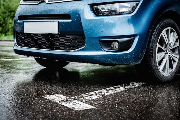 Cerca de la parte delantera del auto azul en el estacionamiento en un día lluvioso.