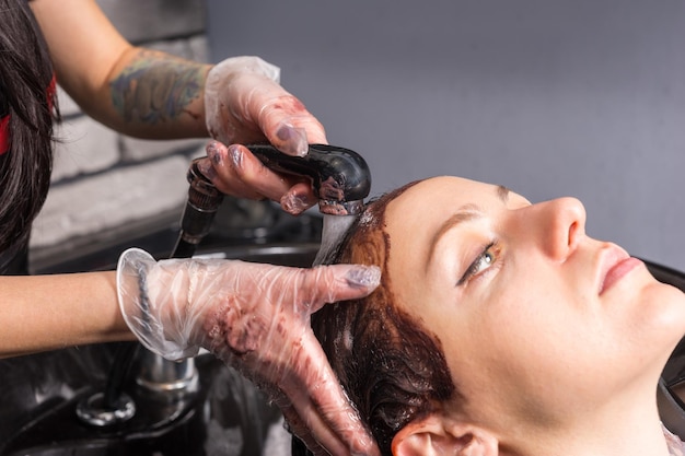 Cerca de peluquería lavarse el cabello de la clienta con el cabello teñido en el lavabo de lavado en el salón de belleza