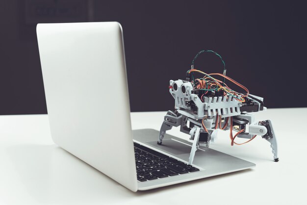 De cerca. Pequeño robot gris con ordenador portátil en la mesa.