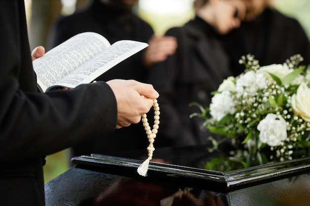 Cerca de una persona de negro rezando en un funeral al aire libre y sosteniendo una biblia con espacio para copiar rosario