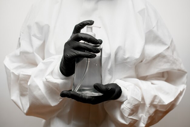 Foto de cerca. persona en ropa de protección médica blanca con guantes de látex negro tiene desinfectante en las manos.