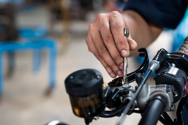 de cerca. Las personas de la mano están reparando una motocicleta Utilice una llave y un destornillador