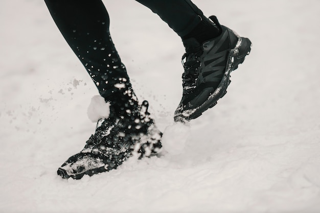 Cerca de pies corriendo en la nieve al aire libre. Ropa deportiva, fitness de invierno, zapatillas