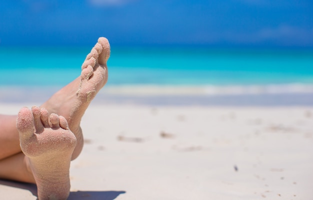 Cerca de pies femeninos en la playa de arena blanca