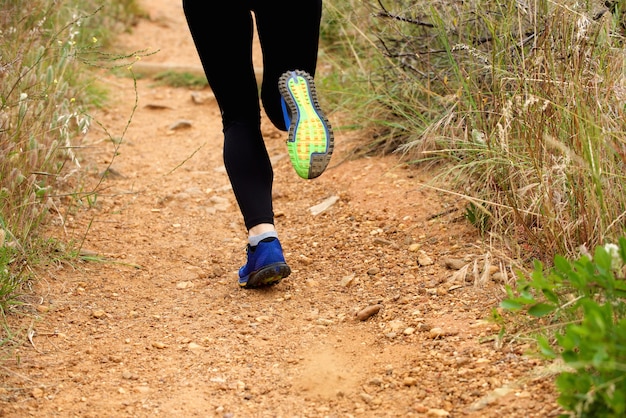 Cerca de los pies de la mujer corriendo en el sendero desde atrás