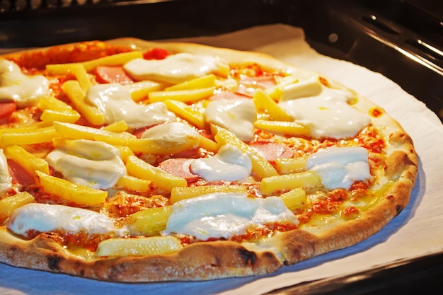 Cerca de una pizza con salchichas y papas fritas en el horno