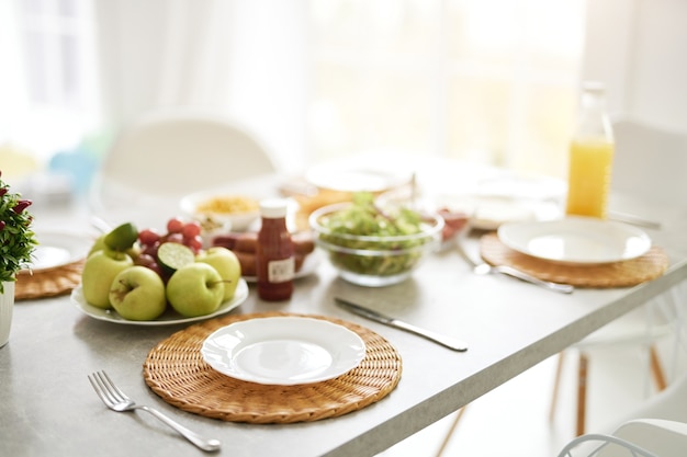 Cerca del plato blanco vacío y desayuno estilo latino sobre la mesa. Interior de cocina blanco brillante moderno con detalles de madera y blanco. Mañana, concepto de ideas de desayuno. Enfoque selectivo