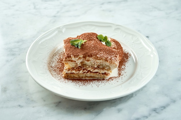 Cerca de una porción de postre italiano tiramisú gourmet servido en un plato blanco sobre una mesa de mármol