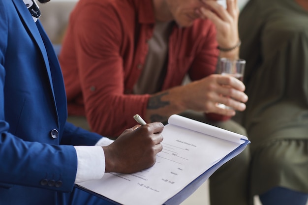 Cerca del psicólogo afroamericano masculino escribiendo en el portapapeles mientras lidera la sesión del grupo de apoyo, espacio de copia