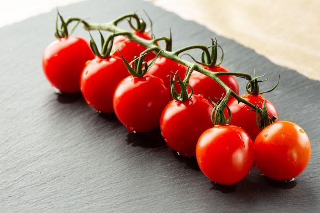 Cerca de la rama de tomates cherry con gotas de agua sobre ellos acostado sobre la superficie de la pizarra negra