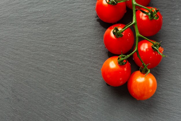 Cerca de la rama de tomates cherry maduros sobre la superficie de pizarra negra