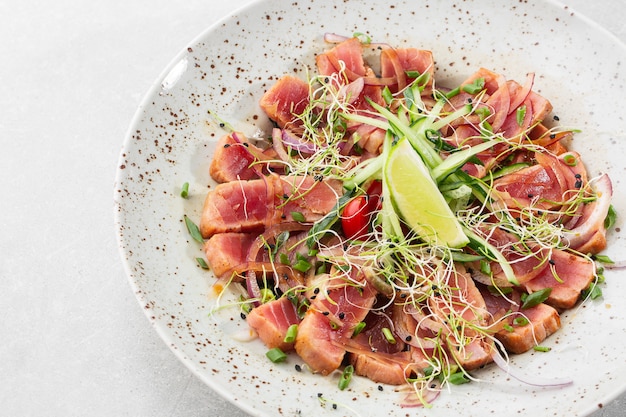 Foto cerca de raras lonchas de atún chamuscado con limón y hojas de rúcula en un plato.