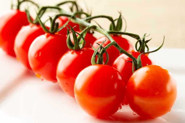 Cerca de la superficie de la mesa blanca y una rama de deliciosos tomates cherry frescos en ella