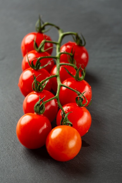 Cerca de la superficie de pizarra negra con una rama de tomates maduros frescos sobre ella