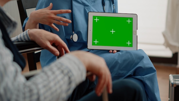 Cerca de la tableta con pantalla verde horizontal de la enfermera. Asistente médico sosteniendo chroma key en el dispositivo con fondo aislado y plantilla de maqueta para pacientes con enfermedades crónicas.
