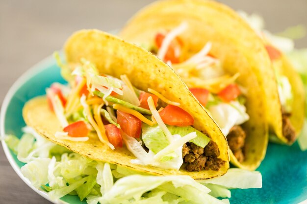 Cerca de tacos de carne fresca en cáscara de taco de maíz amarillo duro con crema agria y queso rallado.