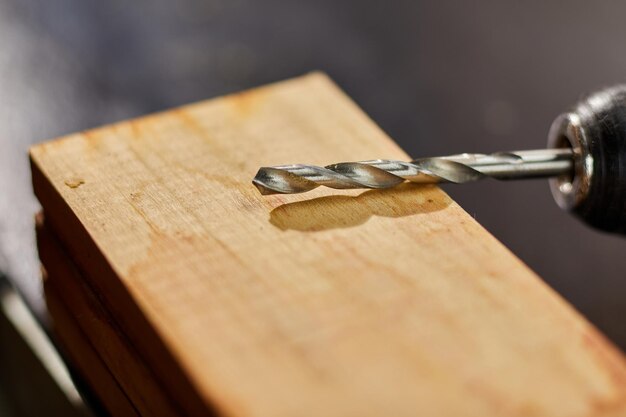 Cerca de taladrar en madera con un tornillo torcido en su lugar broca de metal hacer agujeros en un tablón de robles de madera Hombre Carpente mano taladrar agujeros