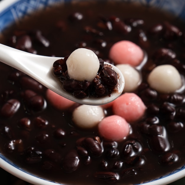 Cerca de tangyuan rojo y blanco (tang yuan, bolas de bola de masa de arroz glutinoso) con sopa de frijoles rojos dulces en un recipiente sobre fondo blanco de mesa para la comida del festival del solsticio de invierno.